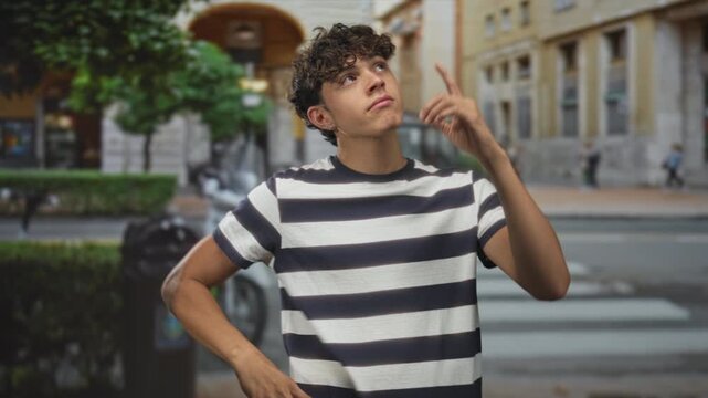 Teen man touching finger to lips for silence on a city street by a crosswalk, arms crossed and eyes closed; thoughtful silence.