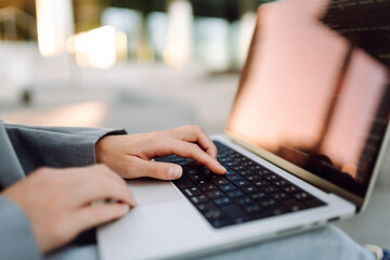 Close-up of a woman's hands typing on a laptop outdoors. A businesswoman enjoys the sunset and her...