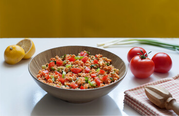 Vibrant bowl of traditional Turkish kisir (bulgur salad) with tomatoes, parsley, and spring onions. Lemon halves and fresh ingredients create a colorful, healthy Mediterranean meal stock photo.