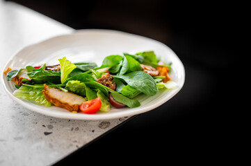A healthy, gourmet grilled chicken and spinach salad with fresh tomatoes and crunchy nuts, served on a white plate with a shallow depth of field