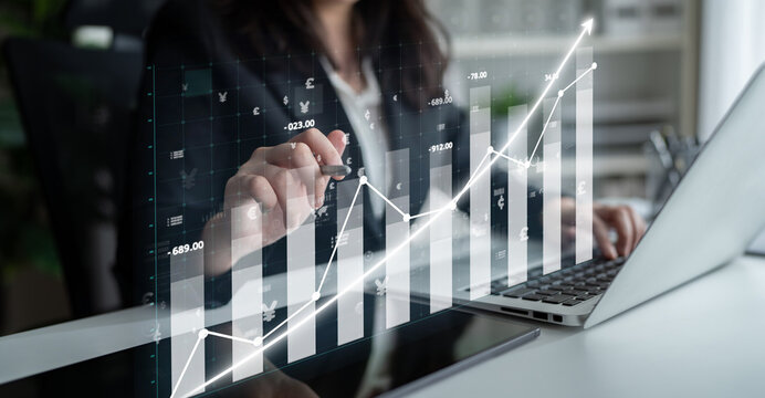 A business professional engages in financial analysis using a digital graph displayed on a laptop, illustrating trends and progress in the modern office environment. Impute