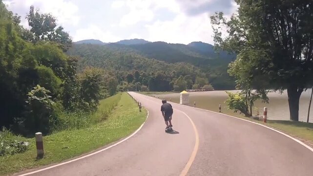 video of man surfskating on a winding sunny road surrounded by green landscape in relaxed motion
