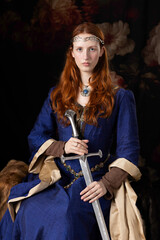 Medieval woman wearing a blue silk dress and holding a sword