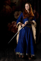 Medieval woman wearing a blue silk dress and holding a sword