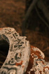 A detailed close-up of a weathered, chipped clay pot with peeling paint and textured surface, resting on a forest floor covered in dry pine needles.