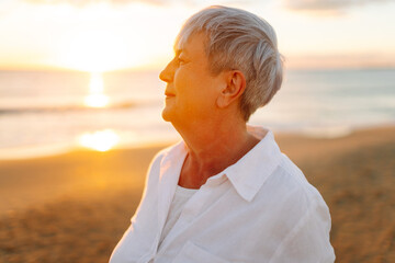 A joyful elderly woman feels free as she strolls along a sandy beach at sunset. Beautiful woman...