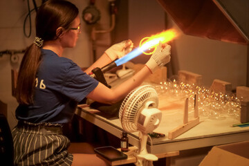 A young girl blows glass toys for the Christmas tree. Glass blower at a Christmas tree decorations factory. Fire and glass..
