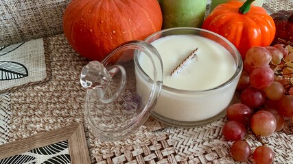 Autumn home decor featuring a scented candle with seasonal fruits and pumpkins on a textured surface