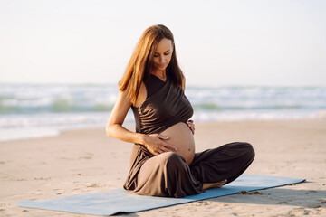 A pregnant woman stretches on a yoga mat by the sea at sunset. A beautiful woman expecting a child meditates or stretches outdoors, enjoying the seascape. The concept is relaxation and rest.