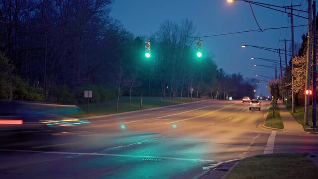 Hyperlapse timelapse time lapse as motion and blurred lights pass by at suburban traffic light intersection with fast moving cars over long period of time during night and dusk near Central Ohio roads