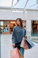 Young woman confidently walking through a bright shopping mall, happily carrying several colorful bags after a successful retail therapy session