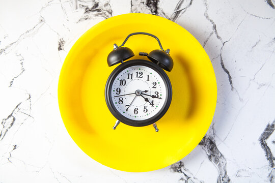 Alarm clock on a yellow plate on a white marble background.