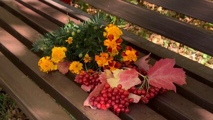 Colorful autumn arrangement of flowers and leaves on a park bench in a sunny afternoon