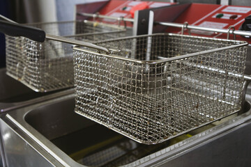 Close-up view of two professional deep fryers featuring stainless steel oil containers and metal frying baskets in a commercial kitchen setting. Clean industrial equipment designed for deep-frying.