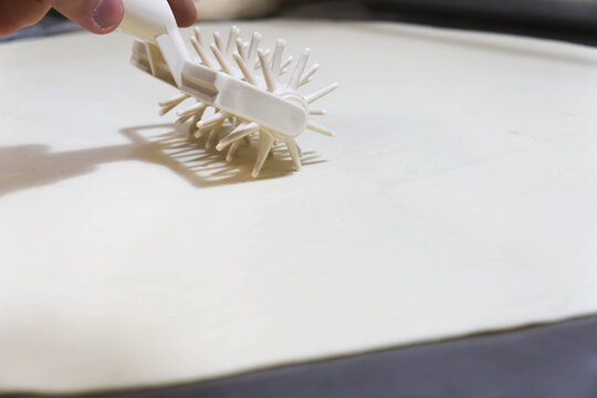 Close-up of a professional dough docker perforating pizza dough to prevent air bubbles during baking. Stainless-steel kitchen tool used in pizzerias and commercial kitchens. Close up.  - Powered by Adobe