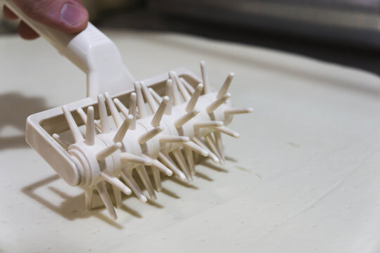 Close-up of a professional dough docker perforating pizza dough to prevent air bubbles during baking. Stainless-steel kitchen tool used in pizzerias and commercial kitchens. Close up. 