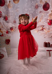 Kleines lachendes M&auml;dchen mit rotem Kleid freut sich &uuml;ber die Weihnachtsgeschenke. 