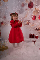 Kleines lachendes M&auml;dchen mit rotem Kleid freut sich &uuml;ber die Weihnachtsgeschenke. 