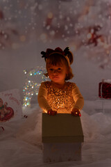 Kleines M&auml;dchen &ouml;ffnet am Heiligen Abend ein Weihnachtsgeschenk, aus dem ein Licht erstrahlt.