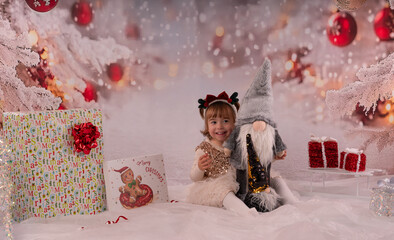 Kleines lachendes M&auml;dchen mit rotem Kleid freut sich &uuml;ber die Weihnachtsgeschenke. 