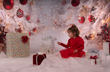 Kleines lachendes M&auml;dchen mit rotem Kleid freut sich &uuml;ber die Weihnachtsgeschenke. 