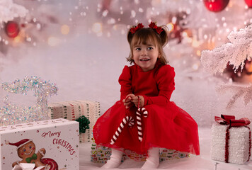 Kleines lachendes M&auml;dchen mit rotem Kleid freut sich &uuml;ber die Weihnachtsgeschenke. 