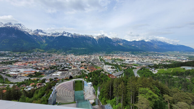Innsbruck, Austria - May 19, 2023. An exciting top view from the Bergisel ski jump stadium to the Innsbruck. In the background is majestic Alps with snow covered tops.