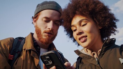 Man shows map on smartphone to African American woman at hiking - Powered by Adobe