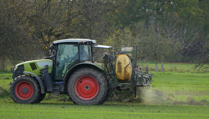 a green farming tractor is spraying fertilizer on a large field in the late autumn