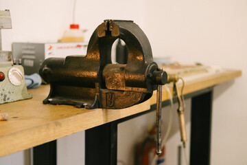 Vise on wooden workbench in workshop, metal clamp tool for repair and maintenance, vintage industrial equipment with worn surface for mechanical and fabrication tasks