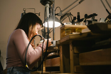 jeweler workshop bench tools lamp soldering craft focused woman working at jewelry bench with rotary tool under lamp making rings with precision and care