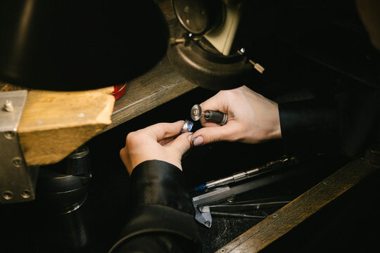 Jeweler jewelry hands working on gemstone with tool at bench in workshop under lamp for precision craftsmanship ring setting polishing repair and manual jewelry making process - Powered by Adobe