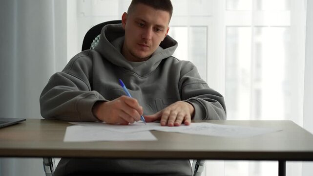A man fills out paperwork in a bright office.
Signing important documents at a desk.
A male screenwriter sits at his desk with a pen in hand.
Work, writing, office, science, education, screenwriter