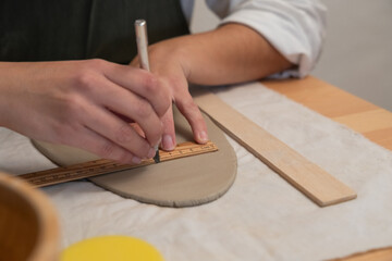 Hands measuring clay with ruler for pottery crafting