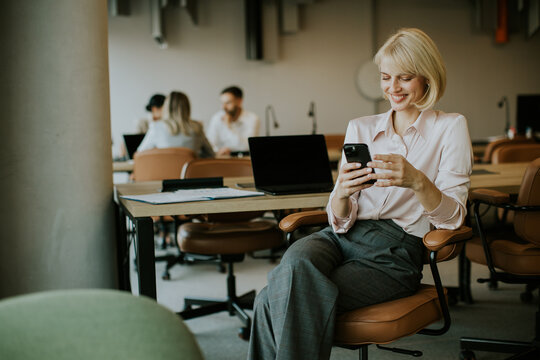 Woman checking her phone while sitting in a modern office environment during the day