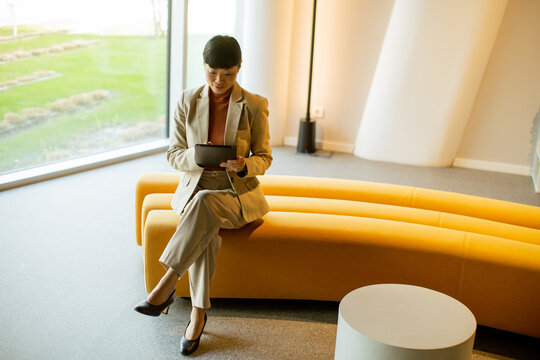 Businesswoman using tablet in modern office lounge area with large windows
