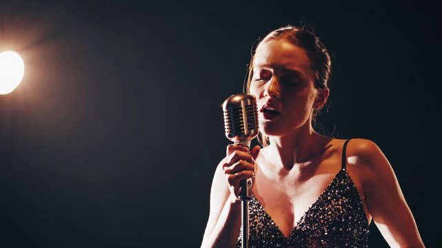 A close-up video still of a singer in vintage style, captured from a low angle with dramatic lighting, highlighting emotion and intensity. - Powered by Adobe