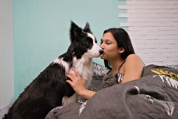 A woman shares a warm moment with her Border Collie as they sit close together on the bed, touching noses or faces, showing affection and a loving friendship.