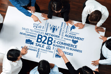 A diverse group of professionals collaborates over a table covered with key business terms,...