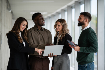Diverse business team collaborating with laptop in office hallway