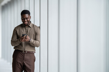 Black businessman smiling texting on smartphone in corridor