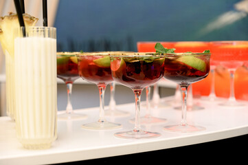 A row of glasses with red cocktails and a tropical milk drink on the bar counter