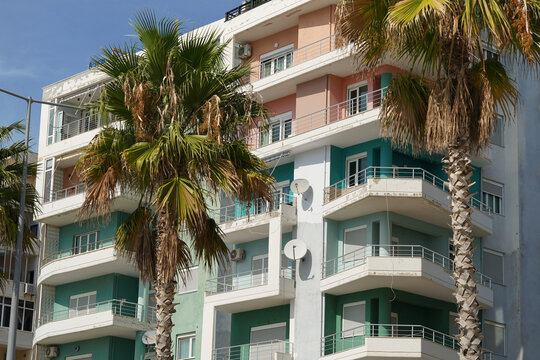 modern balcony building stands along a sunny beachfront promenade lined with palms. Perfect for foreign property investment, long-term rentals, and Mediterranean housing markets. - Powered by Adobe