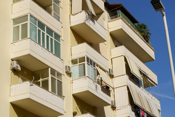 A muted yellow residence with visible AC boxes lines a typical Albanian city street. Perfect for rental seekers, foreign investors, and real estate listings in coastal towns.