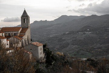Italian church bell tower dominating ancient village homes on a hillside, overlooking a vast rural valley landscape, Agnone, Molise, Italy