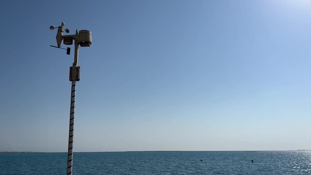 A working anemometer on a pier against the backdrop of the sea and blue sky