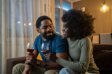 Happy young African American couple enjoying wine at home in living room