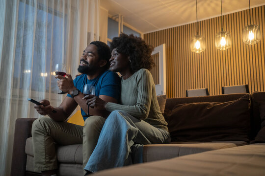 Image of black couple relaxing and watching TV, at home in the evening.