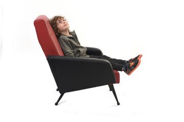 side view of a boy dressed in sportswear sitting in armchair looking up on a white background