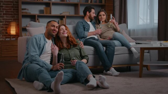 Two multiracial couple in love four diverse friends watching tv at home party together talking Latino men with Caucasian women cuddling discuss film cinema comfortable leisure drink beer double date